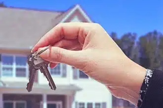 A hand holding pair of keys with a new house in the background. Change the Locks During Divorce