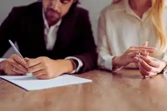a couple sitting at a wooden table, engaged in signing legal documents. Collaborative Divorce vs. Mediation